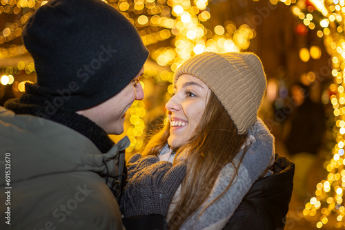 Positive, cheerful couple hugging during x-mas evening. Decorated lights on the streets outdoors (ID: 691532670)
