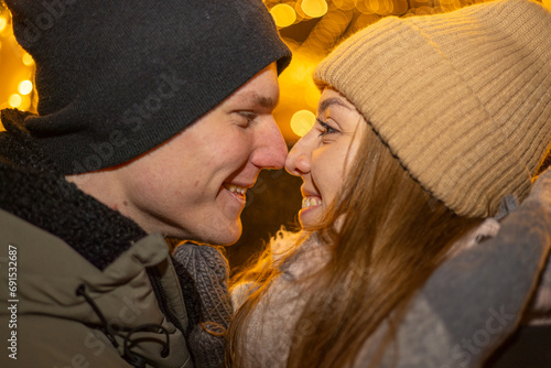 Positive, cheerful couple hugging during x-mas evening. Decorated lights on the streets outdoors (ID: 691532687)
