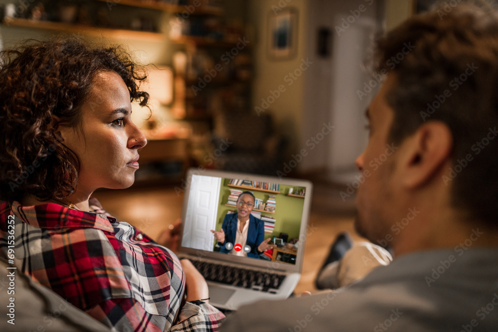 Young couple looking at each other with therapist on video call at home Young couple looking at each other with therapist on video call at home