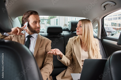 blonde businesswoman talking to handsome man in formal wear calling on smartphone in luxury car