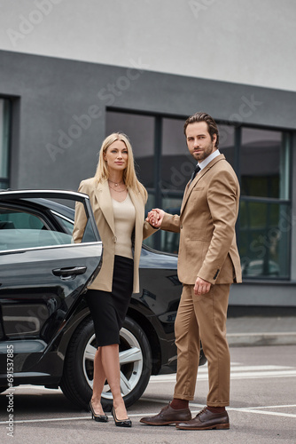 elegant business couple in formal wear holding hands and looking away near car on urban street © LIGHTFIELD STUDIOS