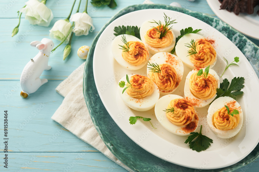 Stuffed or deviled eggs with paprika and parsley on blue plate for easter table. Traditional dish for Easter. Healthy diet food for breakfast. Top view, flat lay.