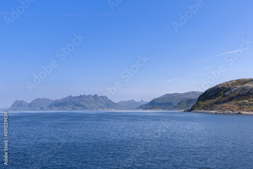 A scenic view of the North Sea and mountains from a ferry heading to Lofoten Island on a sunny summer day, under a blue sky