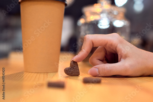 The girl holds a small heart made of cookies with her finger.