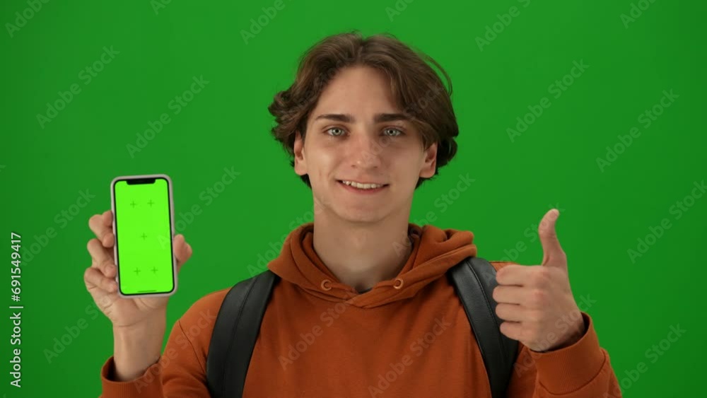 Portrait of traveler isolated on chroma key green screen background. Young man holding smartphone, smiling showing thumbs up at camera. Portrait of traveler isolated on chroma key green screen background. Young man holding smartphone, smiling showing thumbs up at camera.