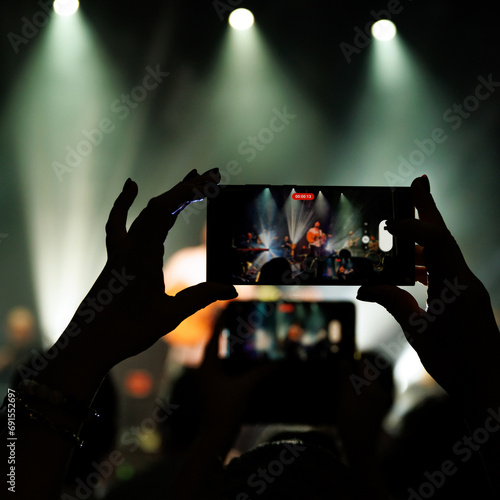 Person recording a concert with their phone. The stage is visible on the phone screen and is lit up.