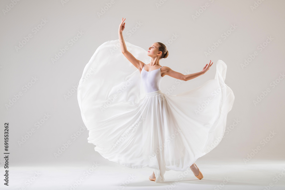 Fototapeta premium young ballerina in pointe shoes dances in a long flying white skirt on a white background