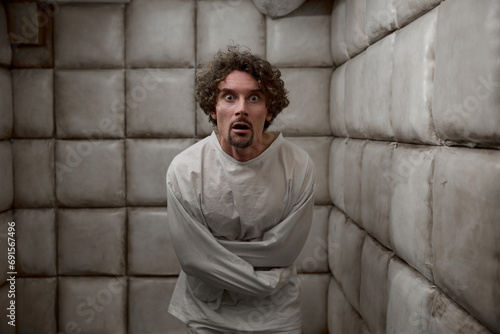 Scared man with schizophrenia mental disorder in white padded room