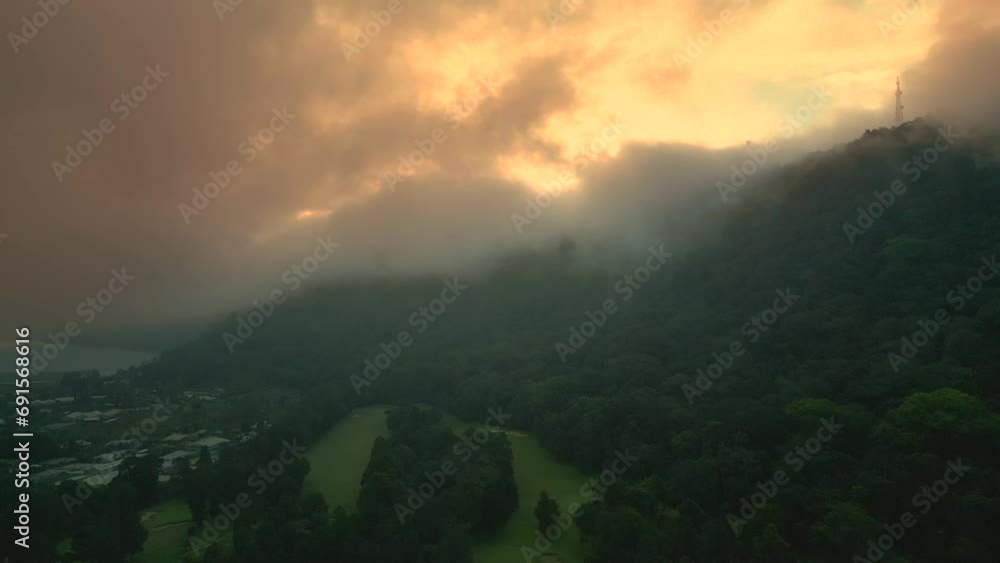 Sunset breaks through the clouds and fog in a mountainous area with dense forest in Bedugul, Bali, Indonesia. Aerial drone view. Sunset breaks through the clouds and fog in a mountainous area with dense forest in Bedugul, Bali, Indonesia. Aerial drone view.