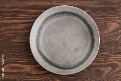 Empty gray ceramic plate on brown wooden background. Top view, copy space