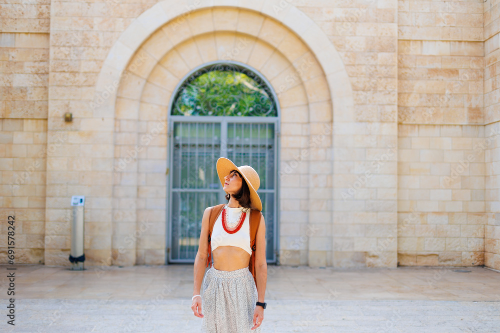 A young girl in a hat and with a backpack walks among old buildings. travel and adventures in Israel. Haifa.