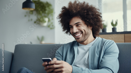 A man sits on the couch at home and smiles holding his smartphone in his hands