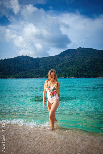 Attractive female in a swimsuit revels in the picturesque scenery of a tropical beach. Crystal-clear turquoise sea and warm sandy shore. Concept of a perfect summer getaway.