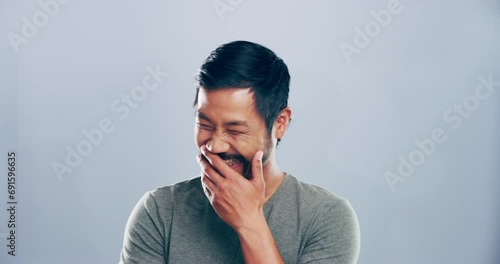 Funny, face and man laughing in a studio for comic or silly joke in conversation with happiness. Smile, portrait and young Asian male model with goofy facial expression isolated by gray background. photo