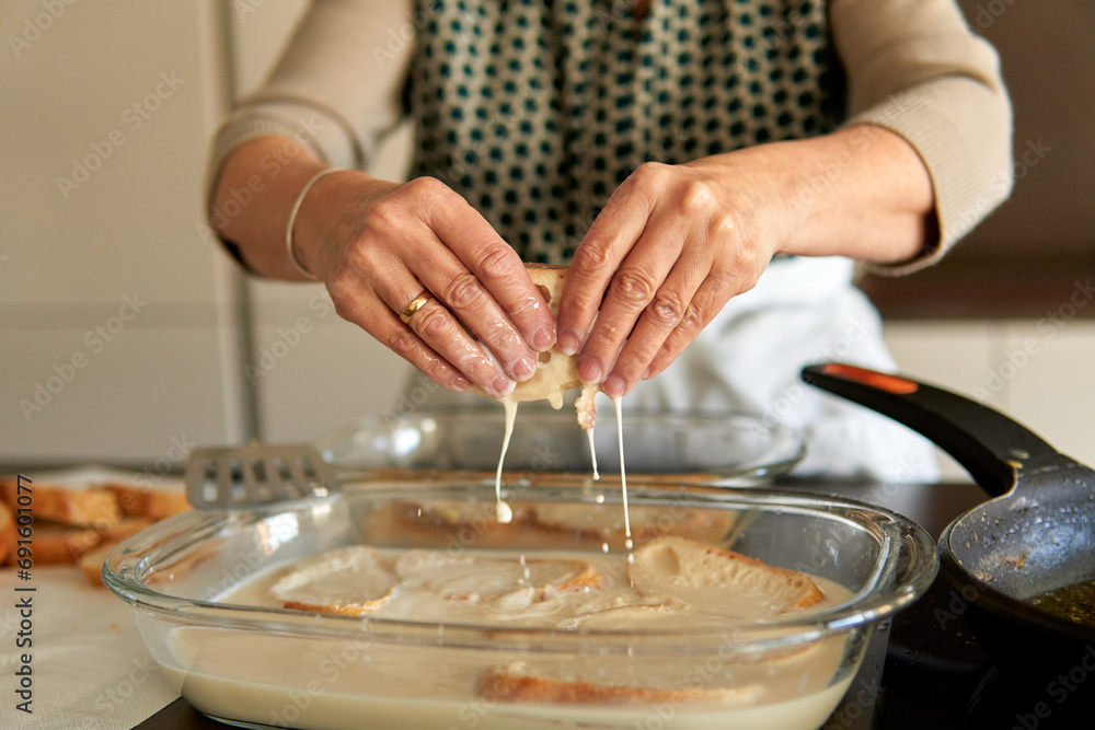 Close up of senior woman hands holding bread with sweet milk and cinnamon to make traditional torrijas recipe. Making traditional recipe on a contemporary electric stove Close up of senior woman hands holding bread with sweet milk and cinnamon to make traditional torrijas recipe. Making traditional recipe on a contemporary electric stove