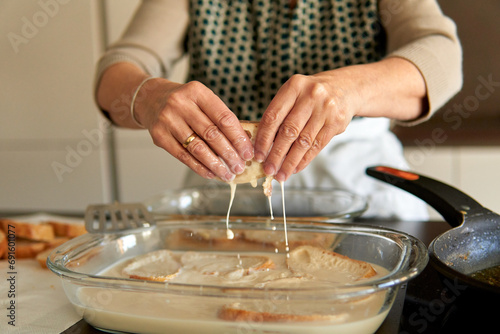 Close up of senior woman hands holding bread with sweet milk and cinnamon to make traditional torrijas recipe. Making traditional recipe on a contemporary electric stove photo