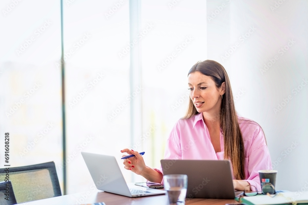 Smiling businesswoman using laptops while sitting at desk and working at a modern office Smiling businesswoman using laptops while sitting at desk and working at a modern office