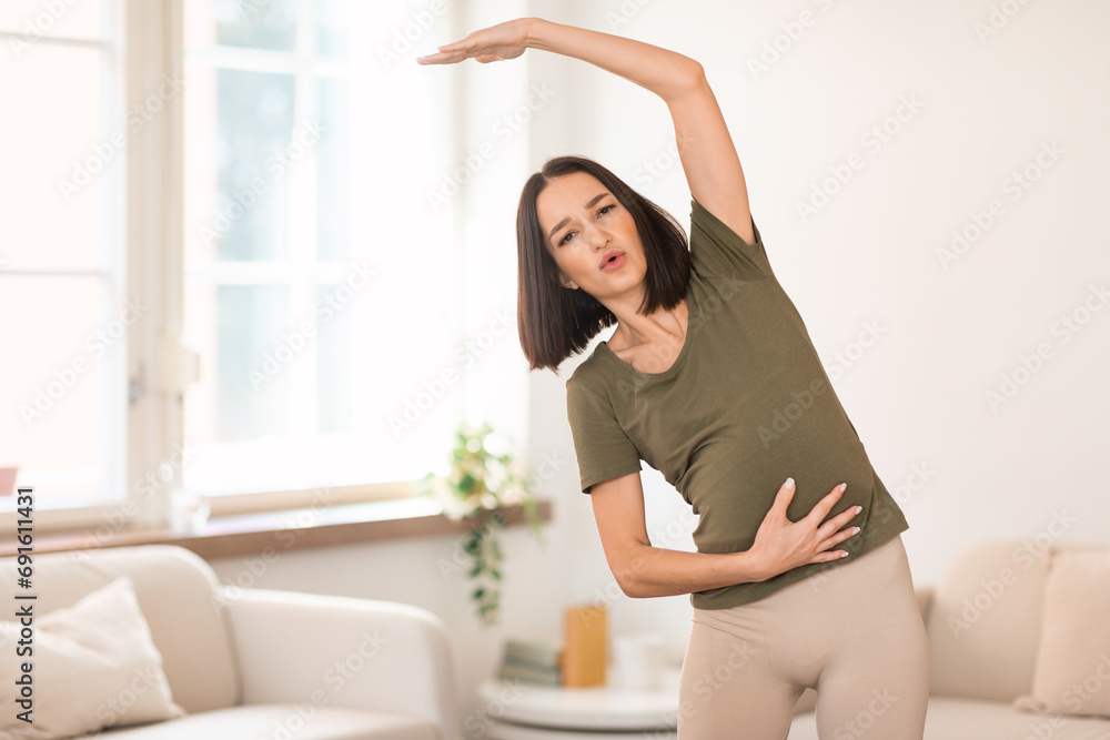 Pregnant lady exercising at home doing side bends raising arm Pregnant lady exercising at home doing side bends raising arm
