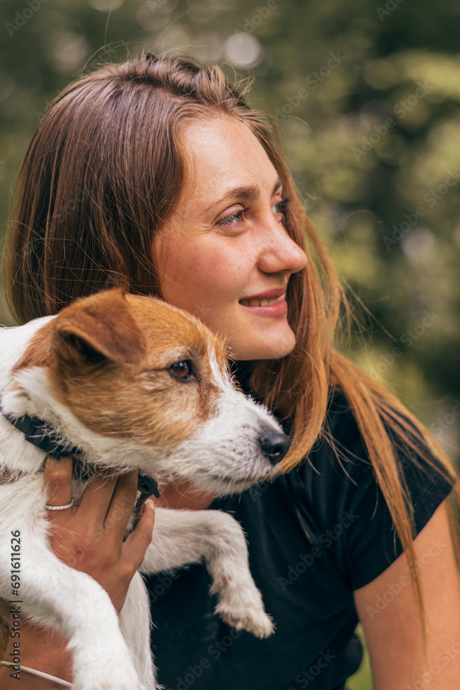 Close-up of a young positive woman hugging friendly Jack Russell Terrier dog, enjoying happy moments together while walking in the park on a summer day. Close-up of a young positive woman hugging friendly Jack Russell Terrier dog, enjoying happy moments together while walking in the park on a summer day.