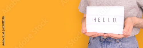 Word Hello. Banner with woman hold in hands lightbox with letters in front of yellow background. Place for text. photo