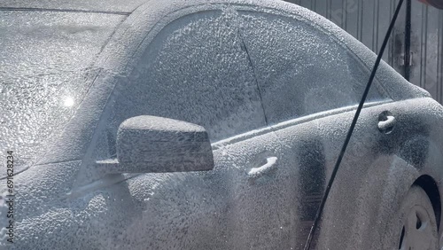 Foam coating of a car with a high-pressure washer. Open car wash. The process of applying soap suds to the sides of a car using a pressure washer - close-up with selective focus. photo