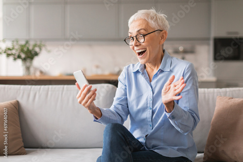 Excited mature lady holding smartphone reading wow online offer indoor