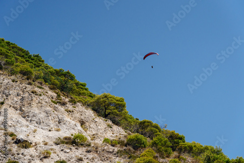 Adventurous spirit captured mid-flight, paragliding over a rugged landscape under a clear blue sky