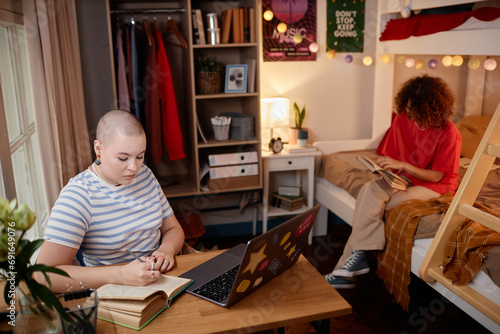 Portrait of two young women studying and doing homework in college dorm room, copy space photo