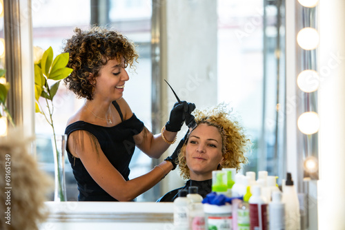 Hairstylist applying color to client's curly hair in a salon photo