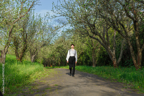 A beautiful girl in a white shirt, in black trousers with suspenders against the background of the sky and green grass