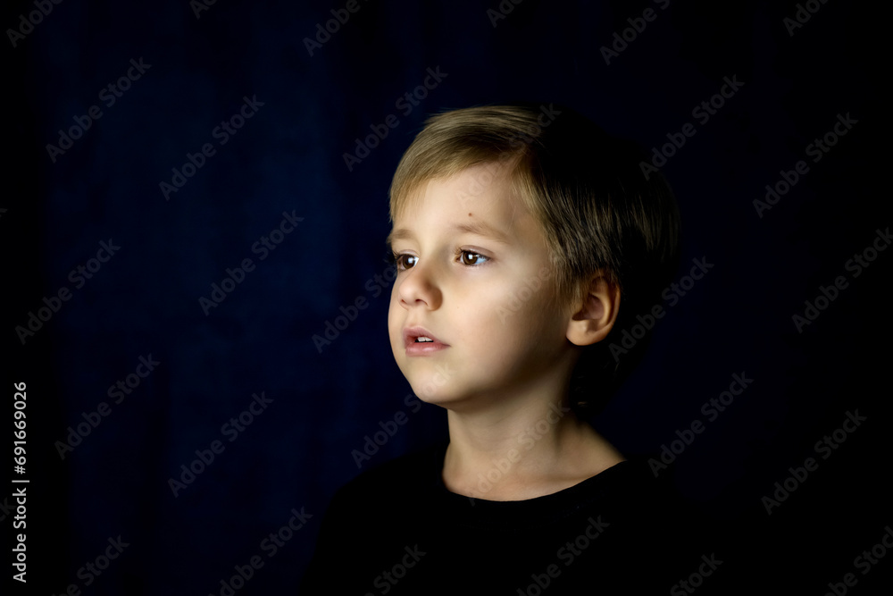 A concise portrait of a European boy. Portrait on a dark background. A concise portrait of a European boy. Portrait on a dark background.