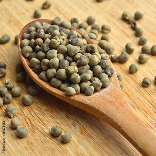 Dried okra seeds in wooden spoon, on bamboo cutting board photo