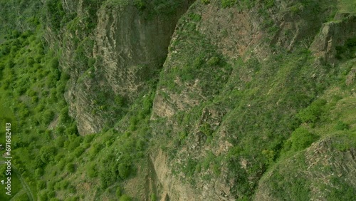 Aerial view of high rocky mountains covered with green grass and trees on a summer cloudy day, with pine trees growing on top. Small villages, country roads. Dzoraget Canyon, Armenia. Drone footage.