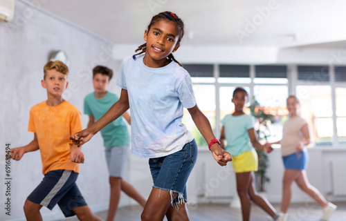Dynamic little boy training Rock-and-Roll dance poses in dancehall with other attendees of dancing courses