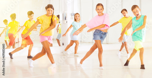 Group of cheerful tween children learning movements of vigorous dance in choreography lesson.