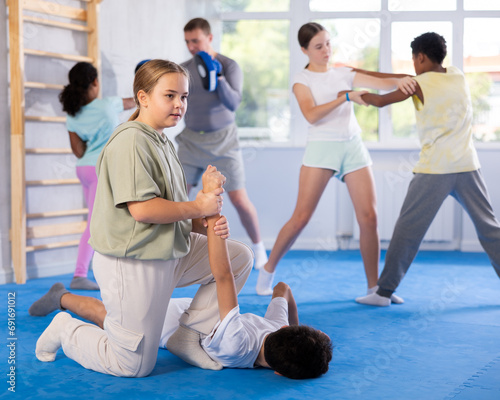 Boy and girl training self-defense techniques in group in studio..