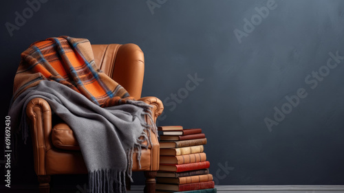 A cozy leather armchair draped with a plaid blanket next to a stack of books photo