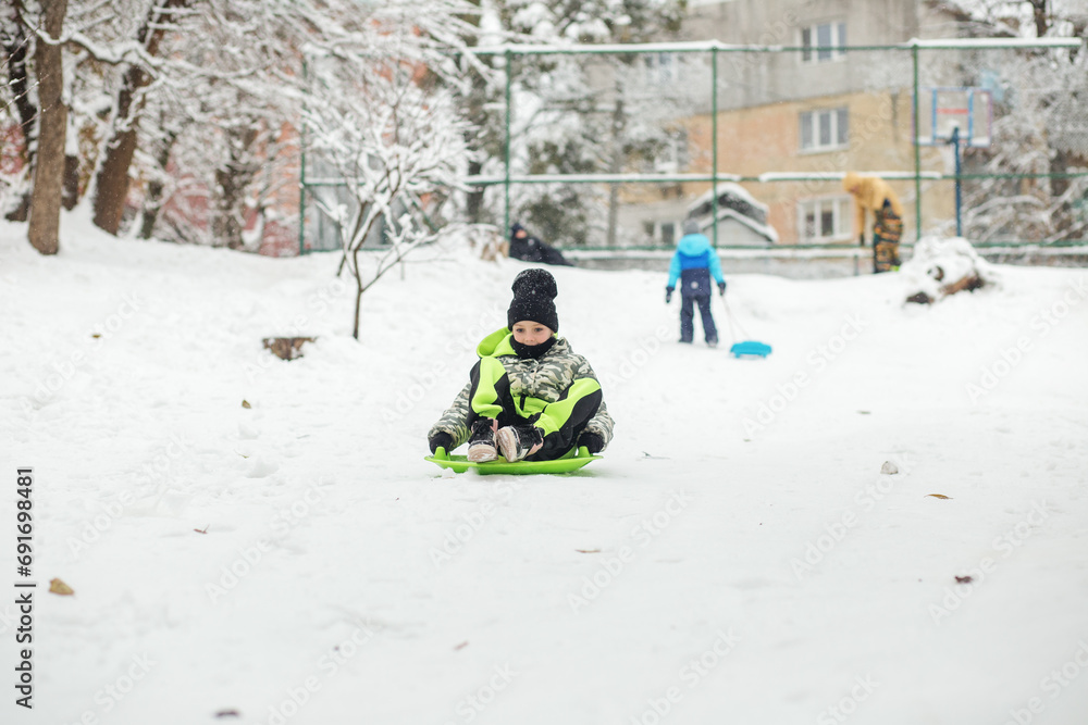 Child girl ride in snow plate. Outdoor play. Cold temperature. Winter time