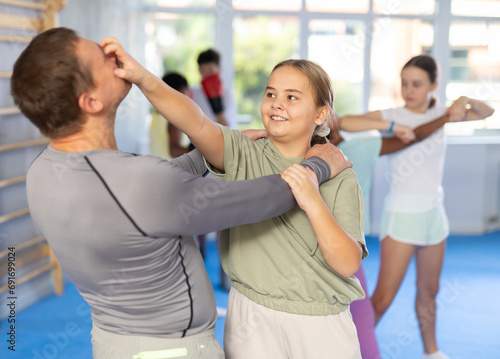Teenage girl practicing basic self-defense moves during mock bout with male instructor in training room, using painful technique to eyes photo