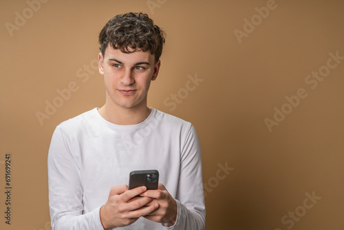 One man caucasian male teenager boy use smartphone mobile phone for online internet browsing social network or sms text messages studio shot beige background happy smile