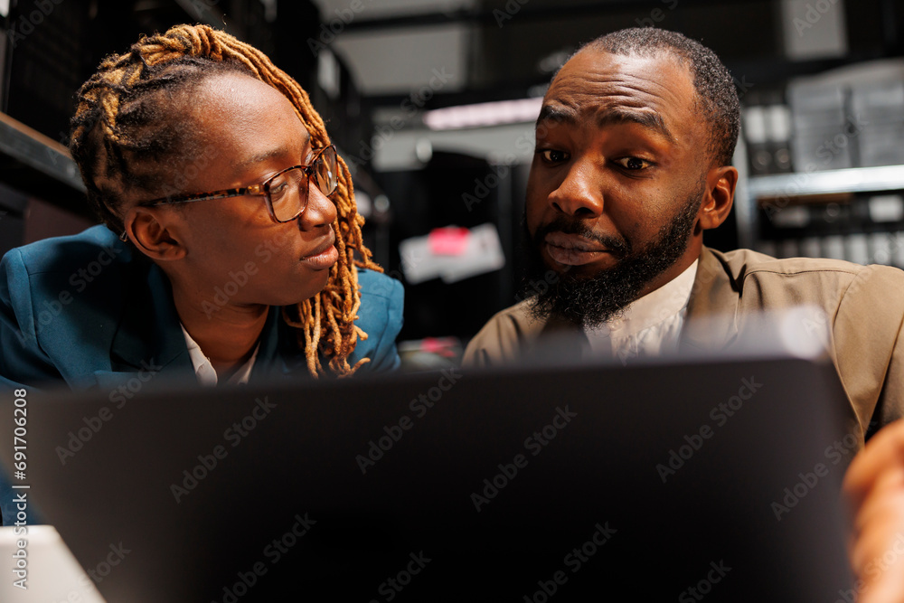 African american detective explaining criminology student crime case analysis in investigation agency office. Investigators analyzing evidence and checking information on laptop African american detective explaining criminology student crime case analysis in investigation agency office. Investigators analyzing evidence and checking information on laptop