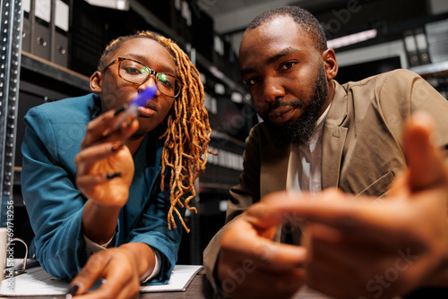 African american man and woman detectives brainstorming and looking at camera. Police investigators partners searching insight for solving crime together in office at night time photo