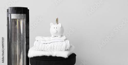 Electric radiator with winter clothes and piggy bank near light wall in room. Banner for design photo
