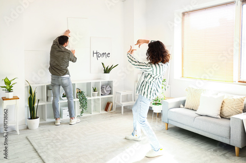 Young couple hanging painting on light wall at home