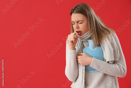 Ill young woman with hot water bottle on red background