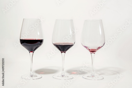 Obraz na plátne Three glasses with less amount of red wine poured in each, isolated on white