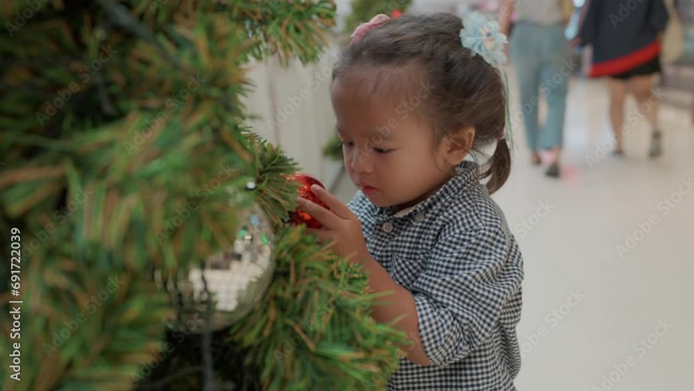 Little asian 2 year girl enjoying decoration gift box ball on christmas tree branch merry xmas happy new year
