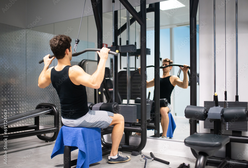 Man using a lat machine in a gym to train his shoulders and back Man using a lat machine in a gym to train his shoulders and back