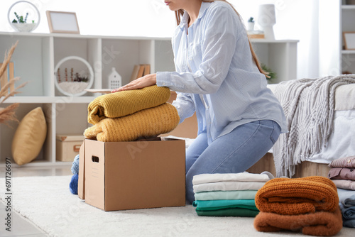 Young woman packing stack of clothes into cardboard box in bedroom photo