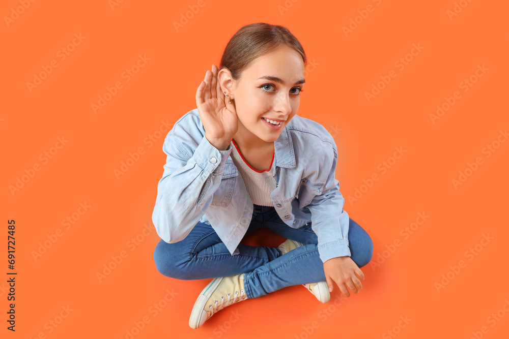 Teenage girl trying to hear something on orange background Teenage girl trying to hear something on orange background
